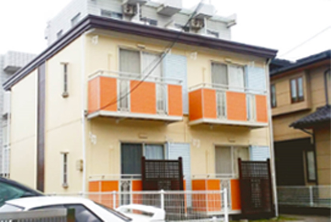 写真：肌色とオレンジの外壁がされている2階建アパート。