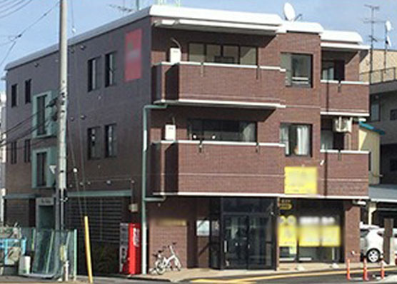 写真:３階建ての建物、1階は店舗、2~3階は住居。茶色の塗装がされている。